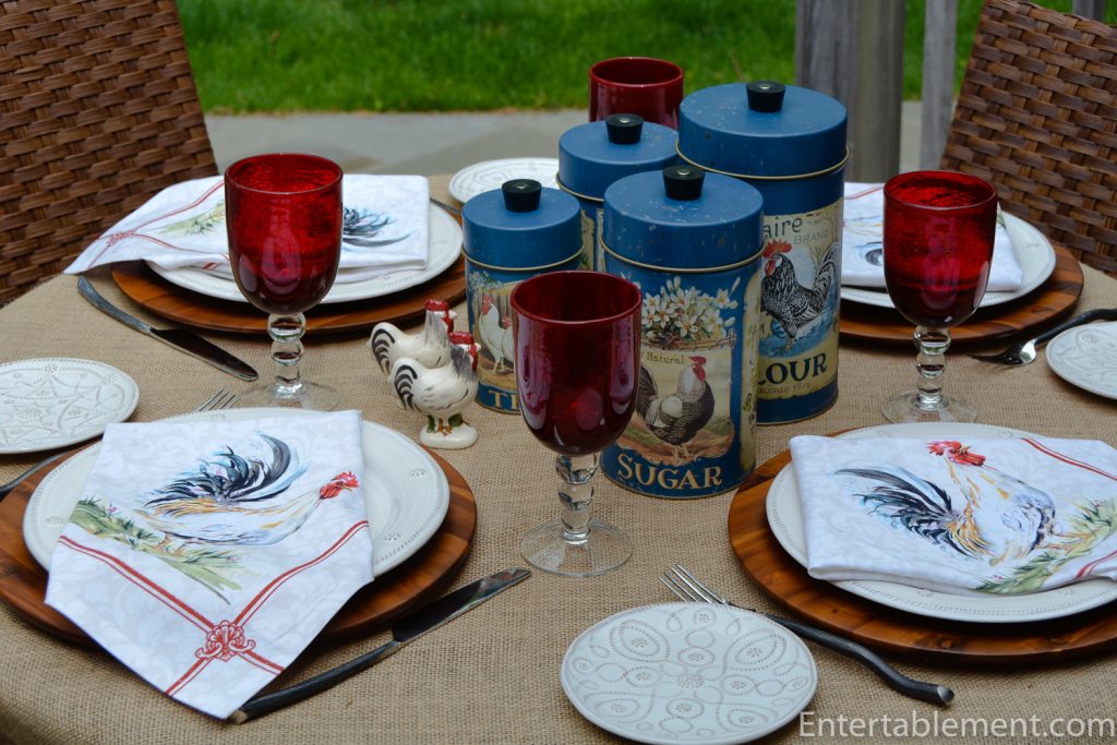 table set with rooster canisters, napkins and red glasses